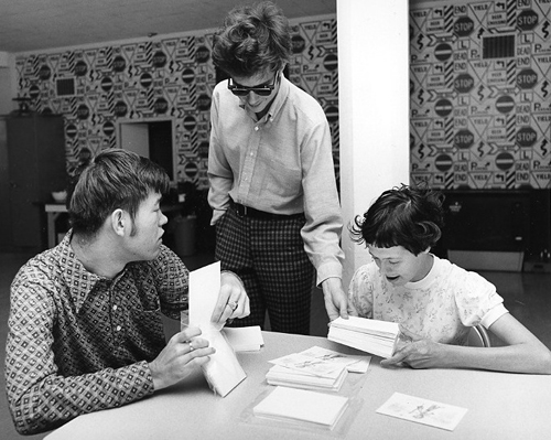 An instructor leans over two children who are reading papers