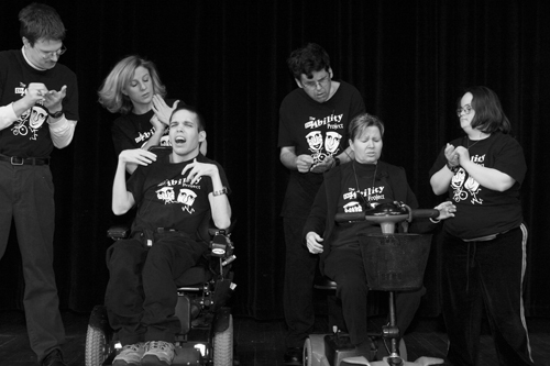 A group of actors, several in wheelchairs, act out a skit
