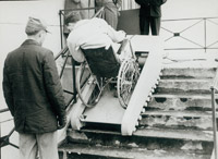 A man in a wheelchair climbs a staircase with the aid of a ramp that moves up the steps with him.